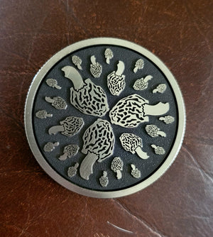Circular metal badge with mushroom design on a brown leather background