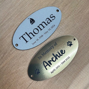 Two oval metal tags, one grey and one gold, with engraved text on a wooden surface.